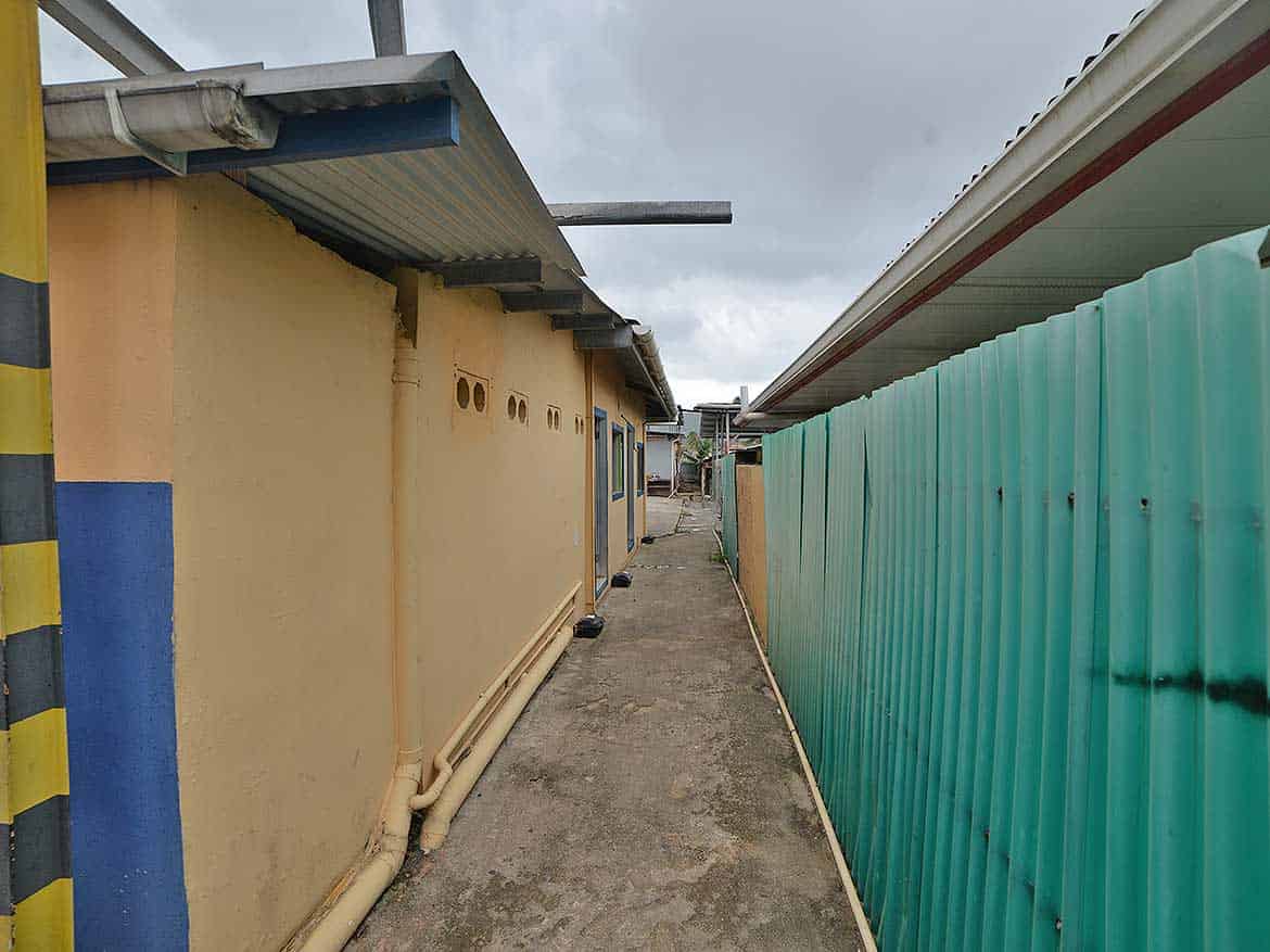 Alleyway near Johnny King Road Cornerstone- Narrow alleyway between buildings with corrugated metal fencing.
