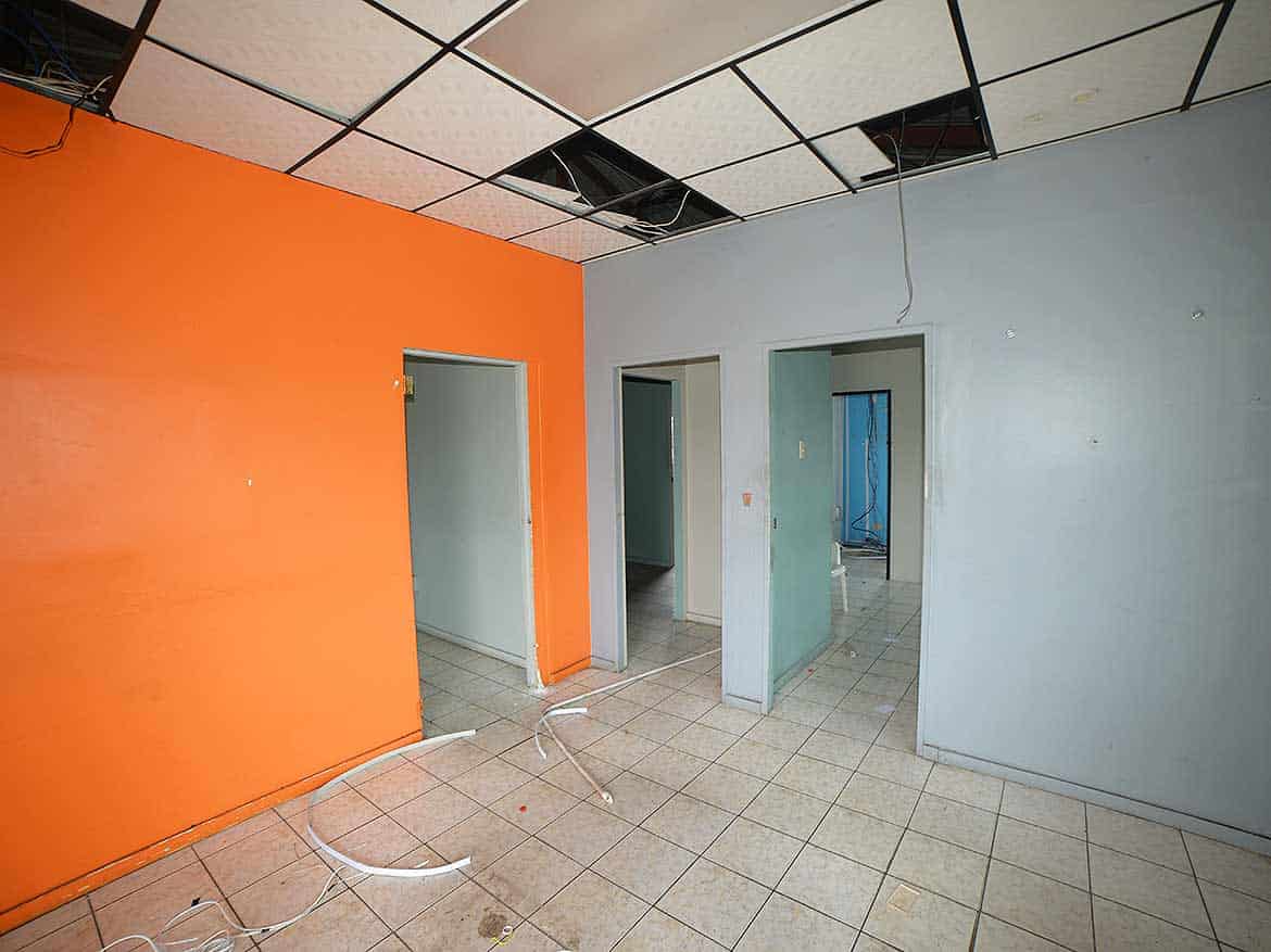 Interior Renovation at Cornerstone Cornerstone- Room with orange and blue walls, ceiling tiles missing, and construction wires.