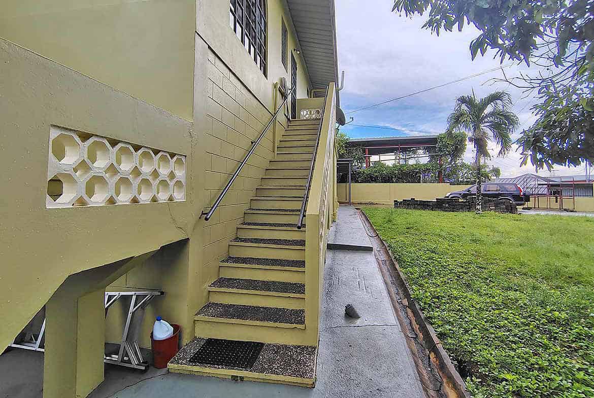 Cornerstone- Exterior view of a yellow residential building with stairs and greenery.