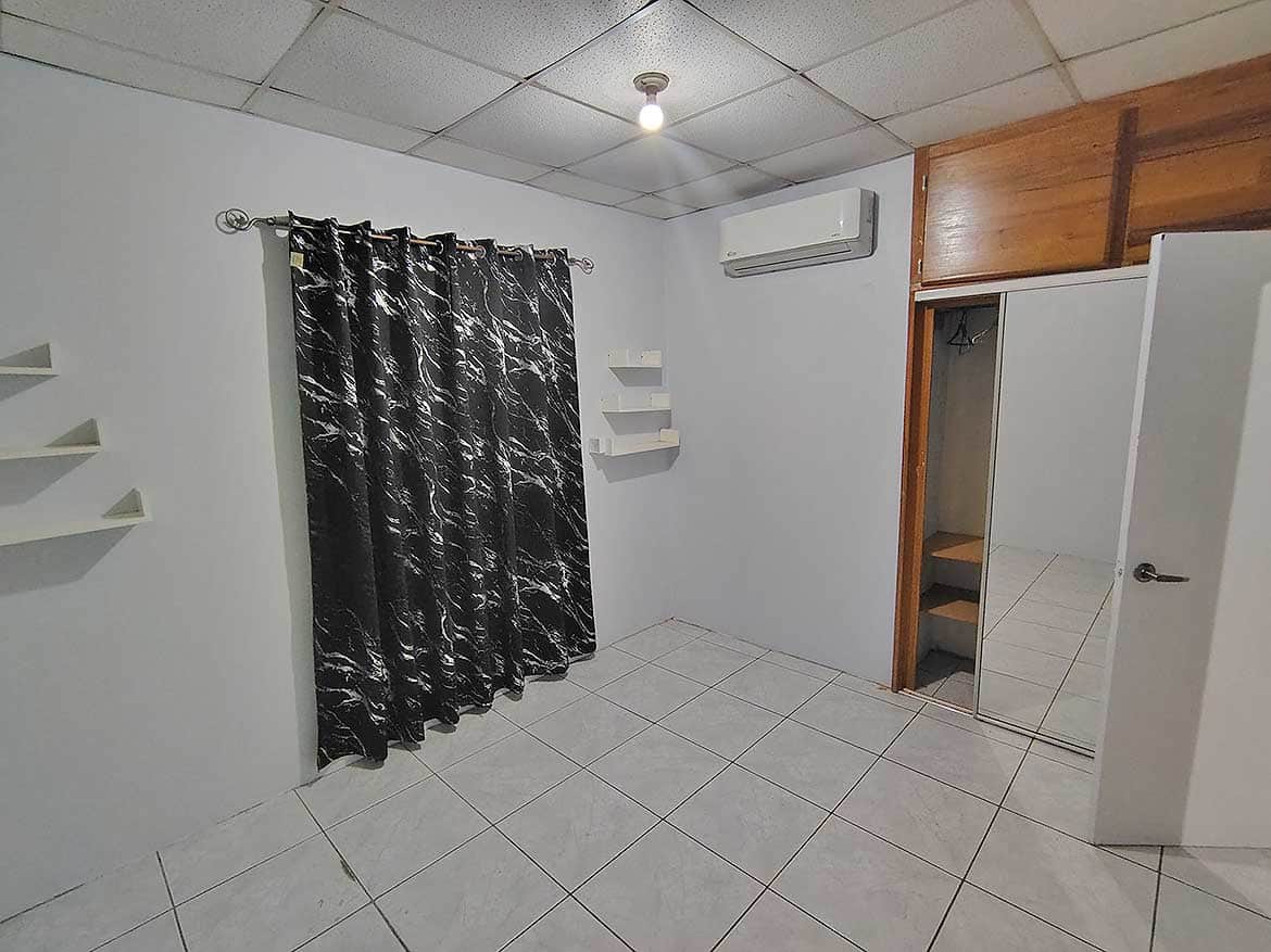 Interior of a Room at Cashew Gardens Cornerstone- Empty room with black curtains, air conditioner, and closet at Cashew Gardens.