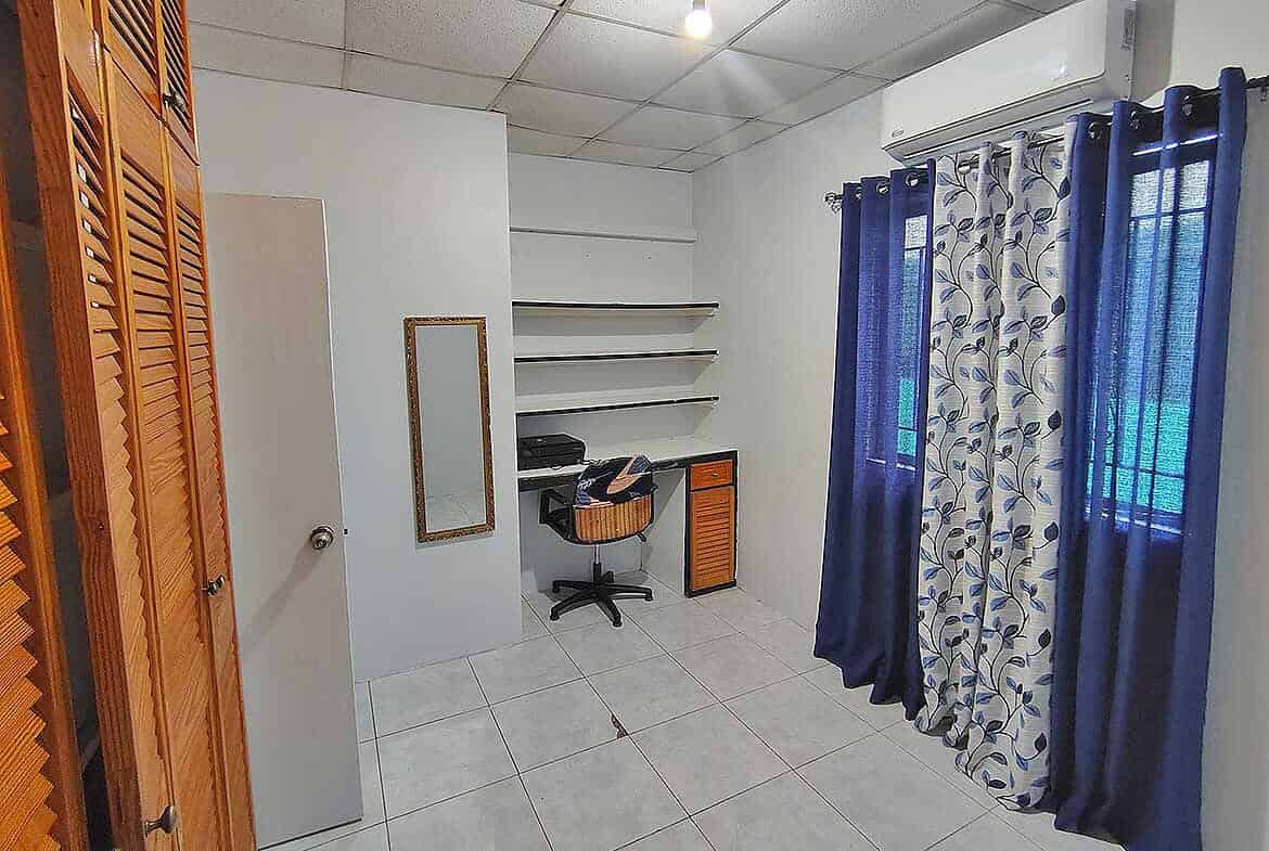 Cornerstone- Room with white walls, blue curtains, and a small desk with shelves.