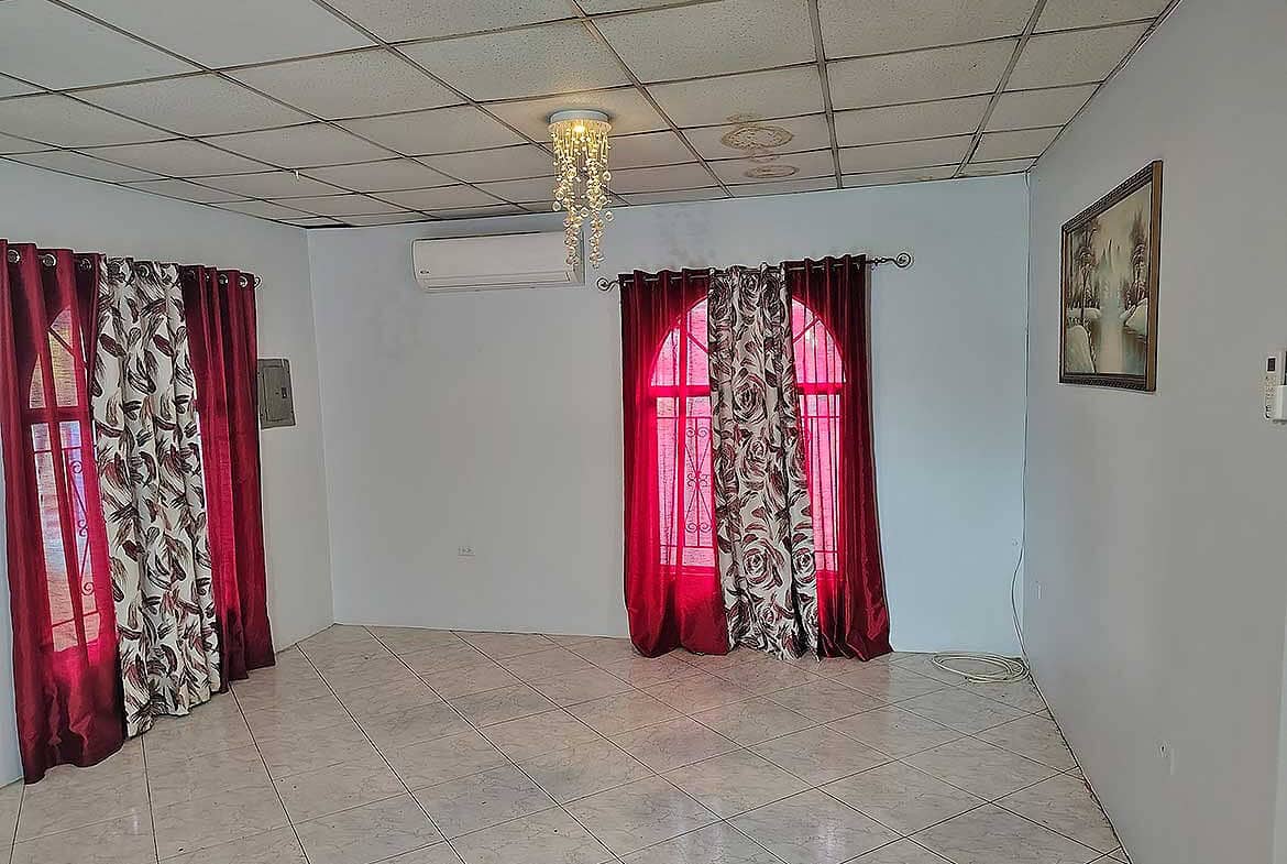 Cornerstone- Spacious room with red and patterned curtains, air conditioning, and artwork.