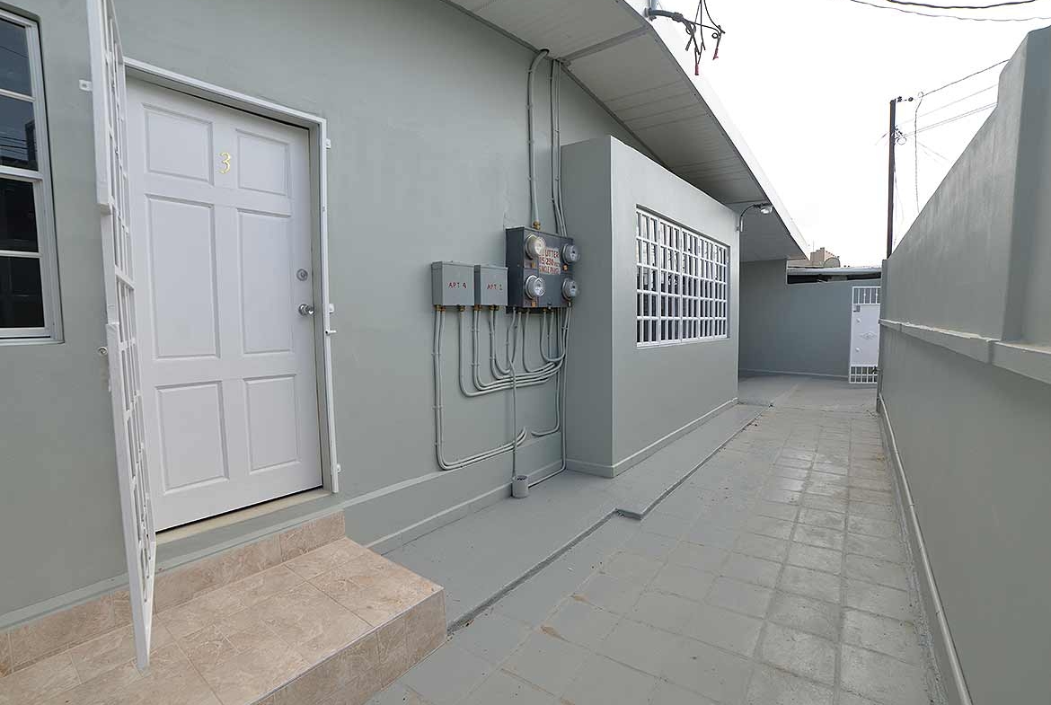 Cornerstone- Exterior view of apartment building with utility meters and door.