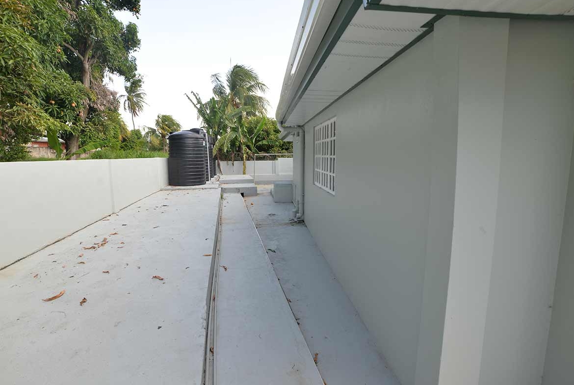 Cornerstone- Side view of apartment building with water tank and lush trees.